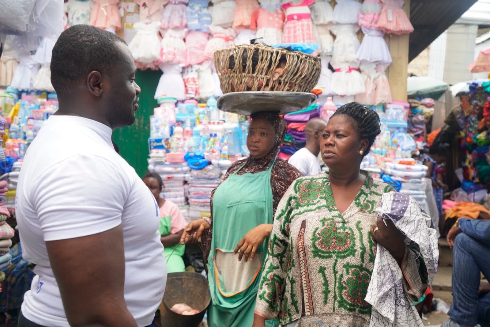 A market street in Ghana, with a woman carrying a basket on her head and stalls of children's clothes behind.